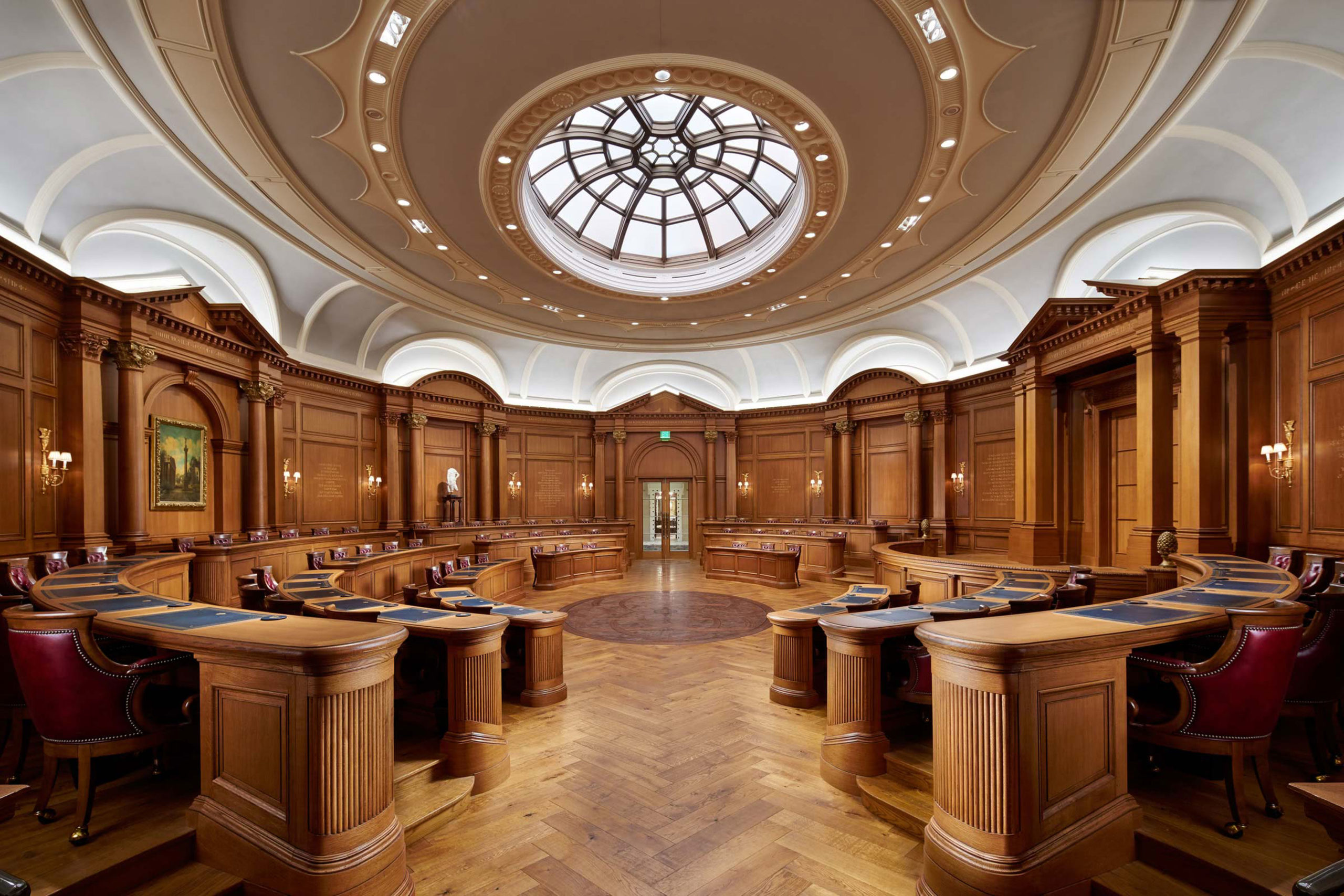 Grand round debate room with wood desks, floors, and walls and a large skylight.